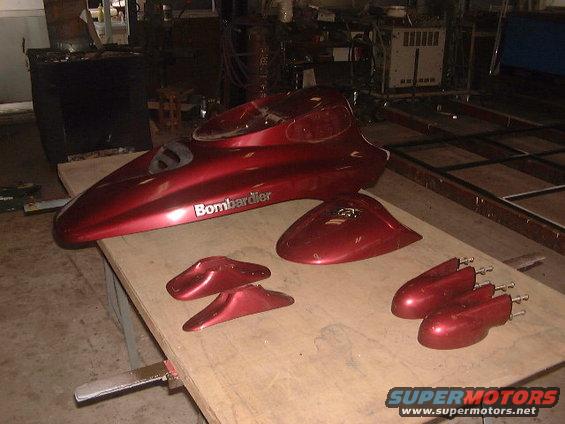 Red Bombardier personal watercraft body panels and hull section on a workbench